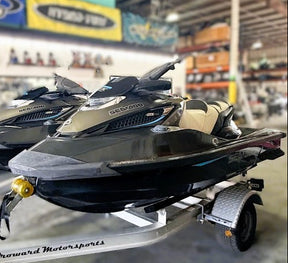 Two jet skis on a trailer in a warehouse setting with various equipment and branding in the background.