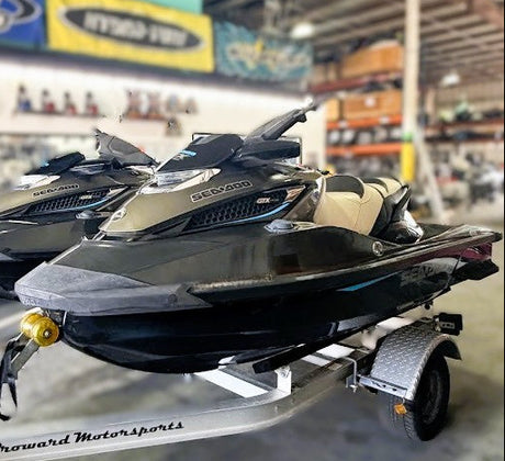 Two jet skis on a trailer in a warehouse setting with various equipment and branding in the background.